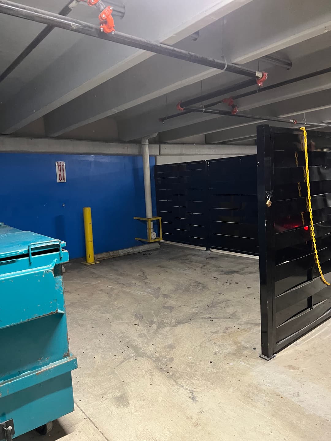 Empty underground parking garage with blue walls and a green dumpster on the left.