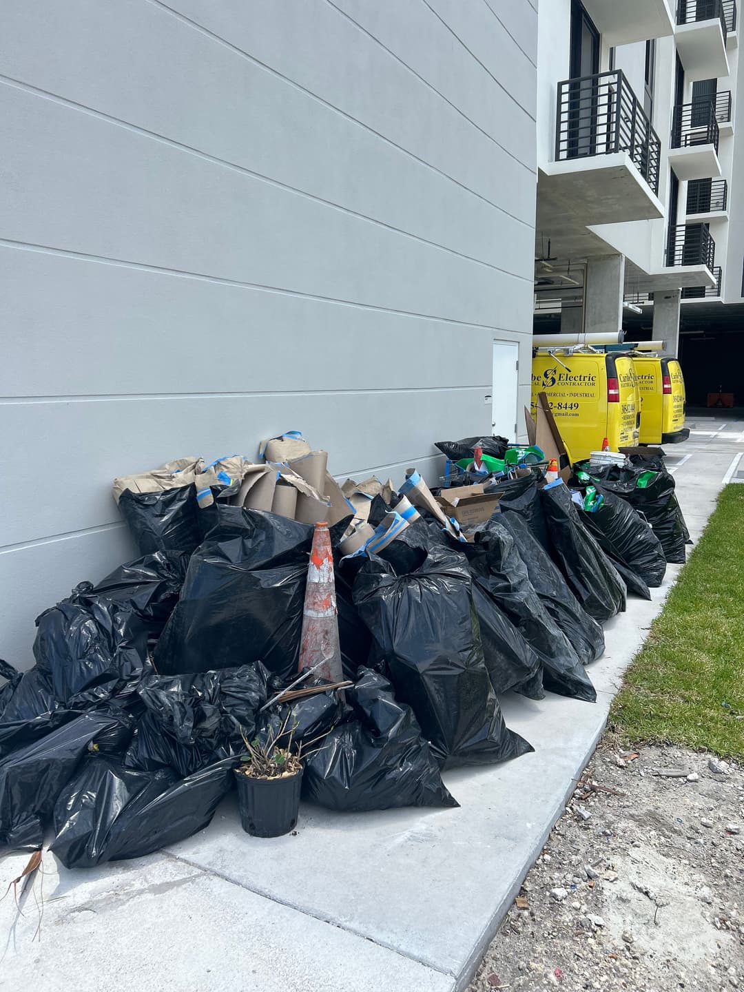 Piles of black garbage bags and recyclables stacked against a building's exterior.