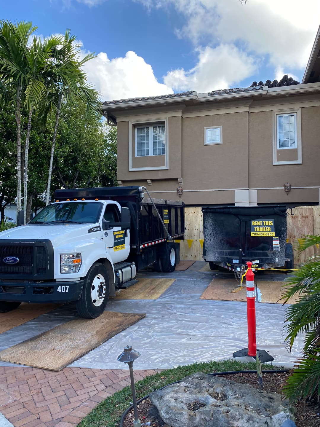Residential landscaping truck and trailer parked in front of a house with palm trees.