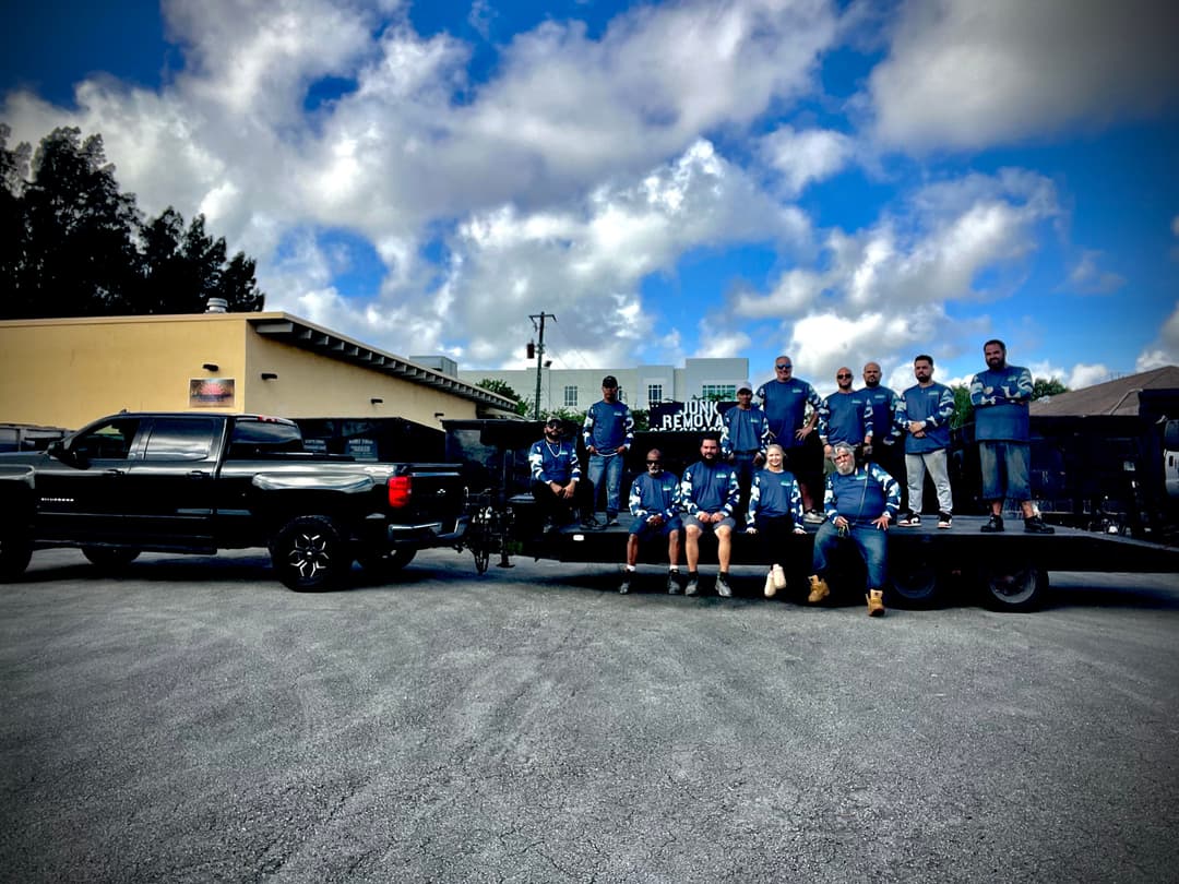 Team of professionals in blue shirts posing by a black truck and trailer under a cloudy sky.