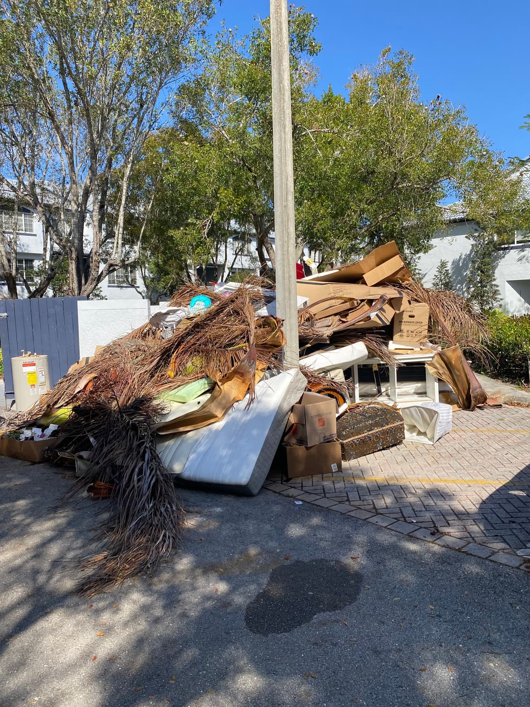 Piled debris and junk including furniture and boxes near a residential area.
