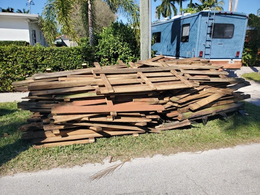 Stacked wooden pallets on a grassy area near a blue camper van in a residential neighborhood.