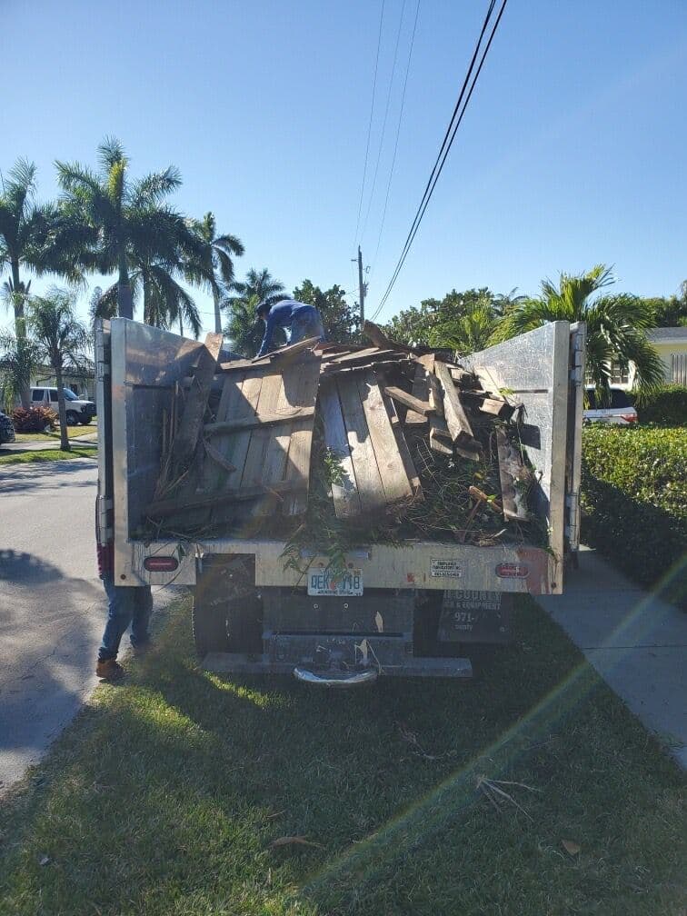 Pickup truck loaded with debris, including wood and yard waste, parked on a sunny street.