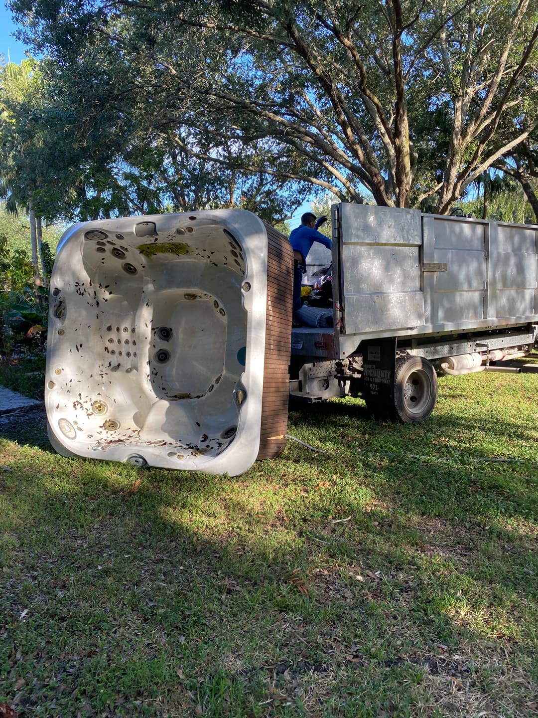 Hot tub being loaded onto a truck for removal amidst lush greenery and trees.