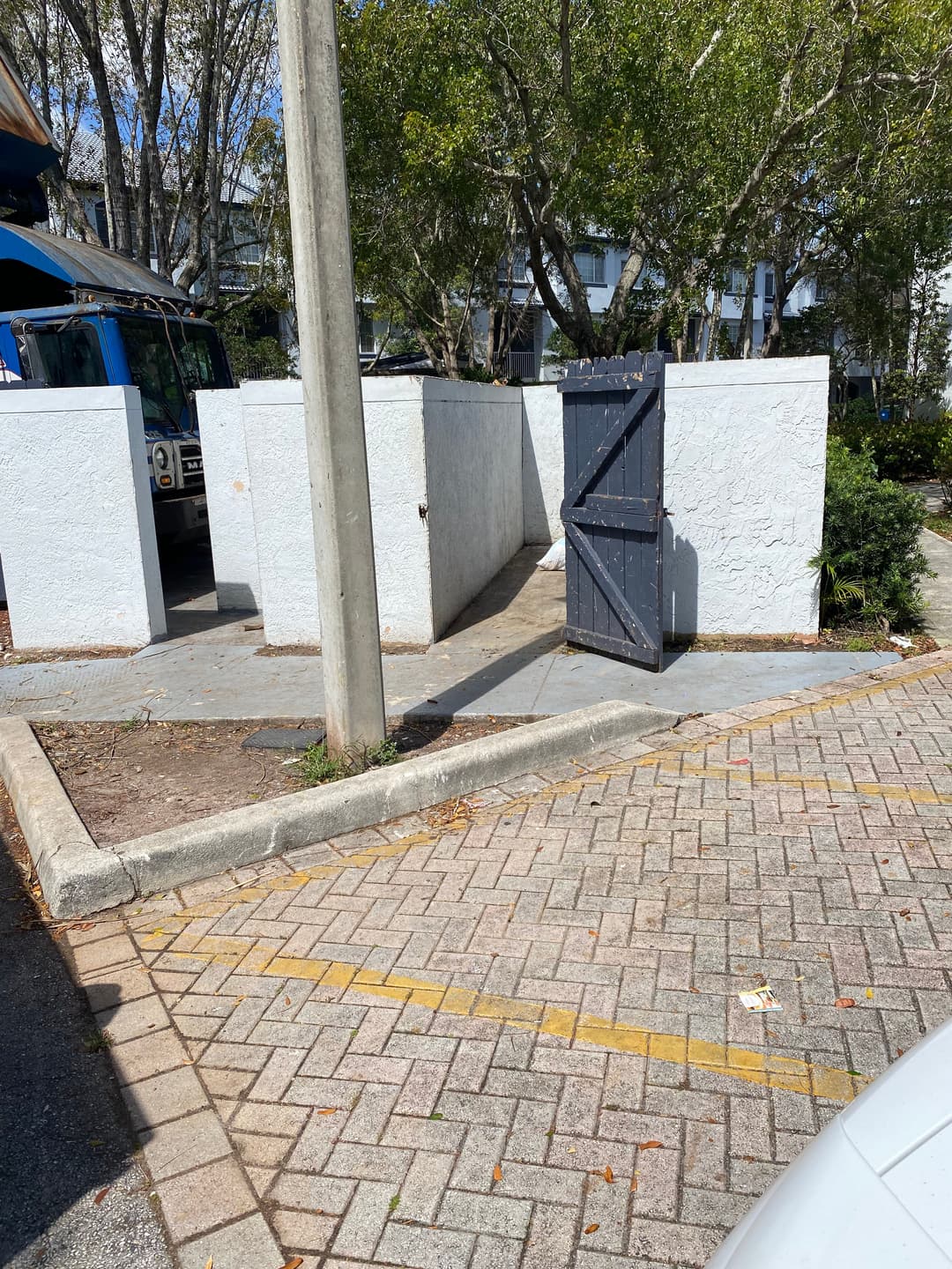 Open black gate in a white-walled enclosure surrounded by trees and parked vehicles.