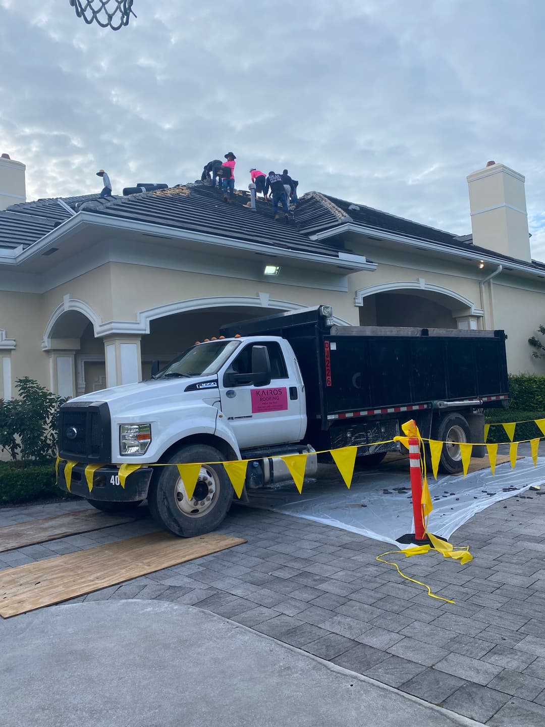 Roofing crew working on a residential roof, with a truck parked nearby and safety equipment in use.
