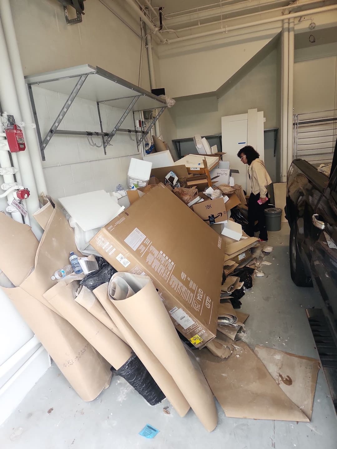 Cluttered garage filled with cardboard boxes and debris, with a person organizing waste.