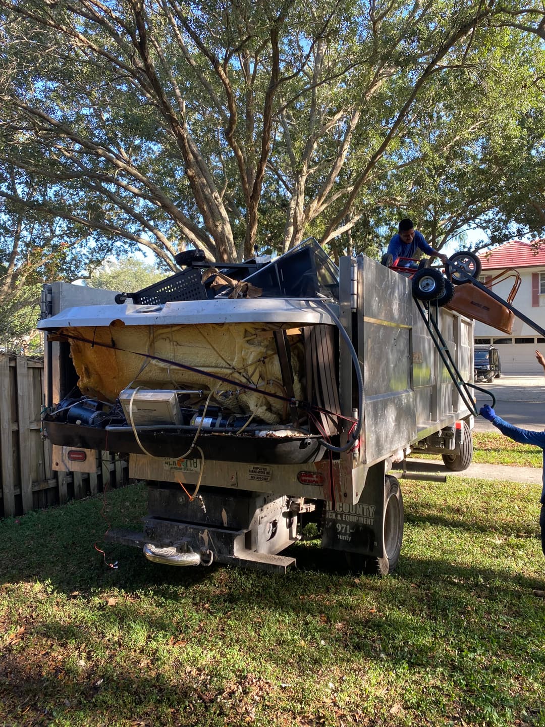Pickup truck loaded with junk and debris for disposal, surrounded by trees and a residential area.