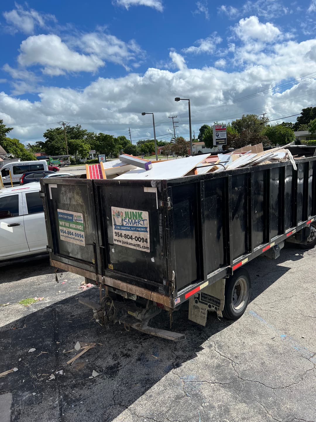 Junk removal dumpster filled with debris near a parking lot on a sunny day.
