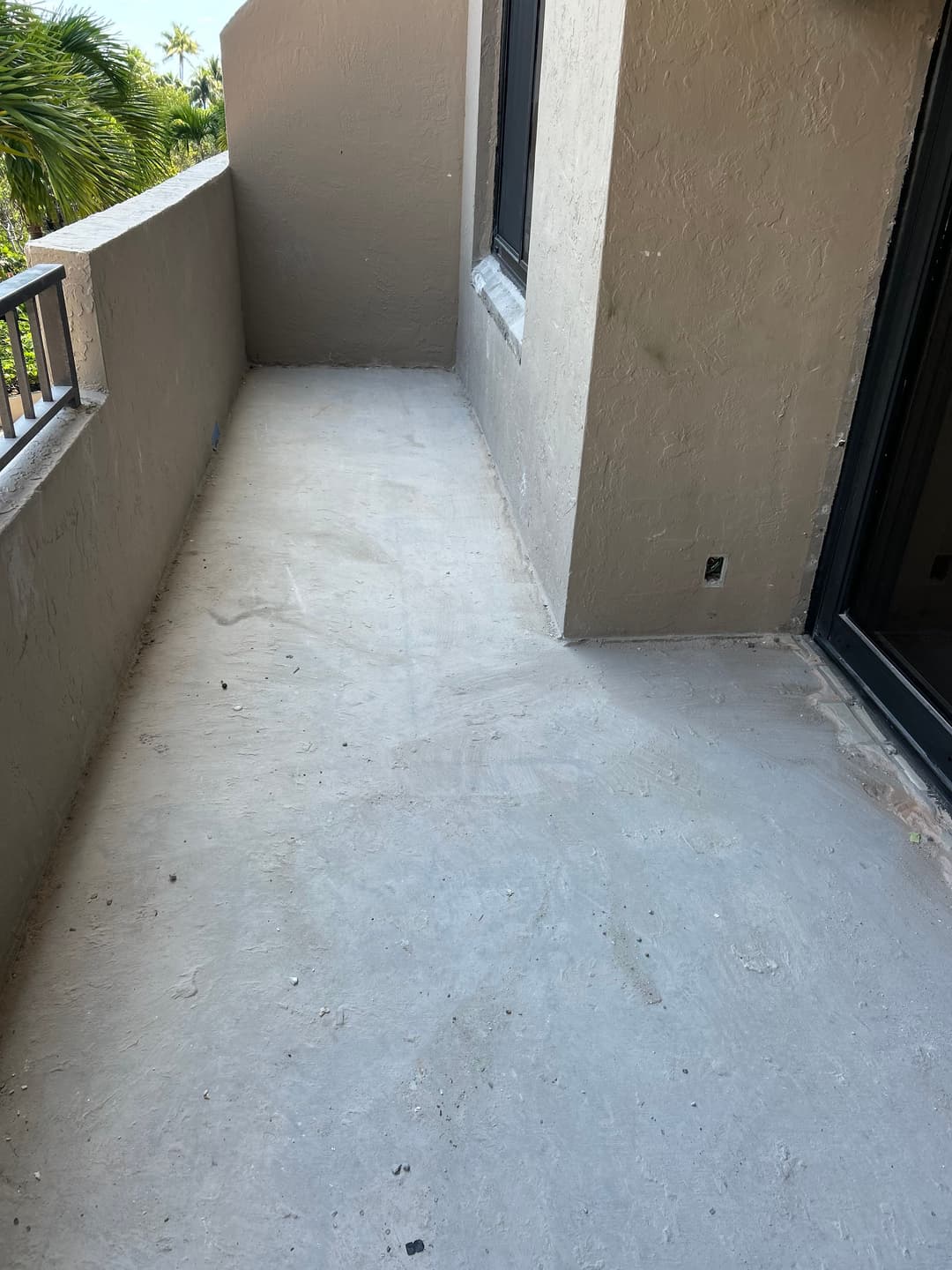 Empty concrete balcony with sunlight, showcasing a spacious outdoor area and tropical surroundings.